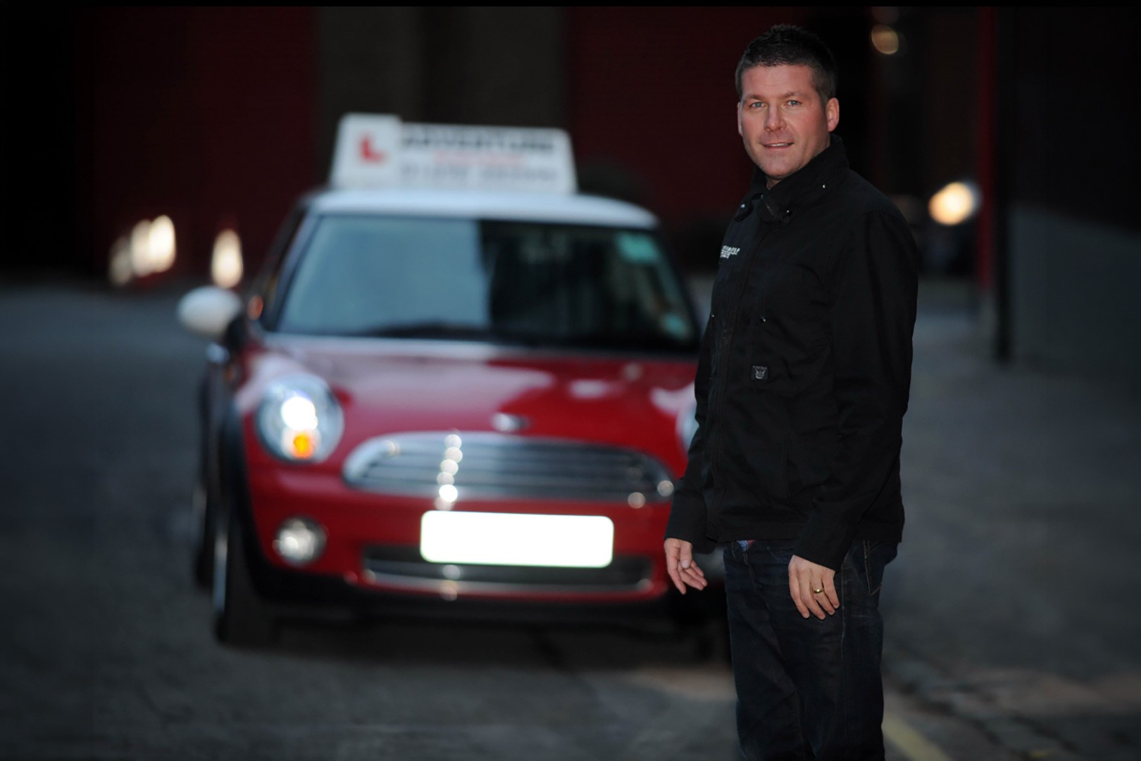 Man standing next to a red MINI with a taxi sign on top at night